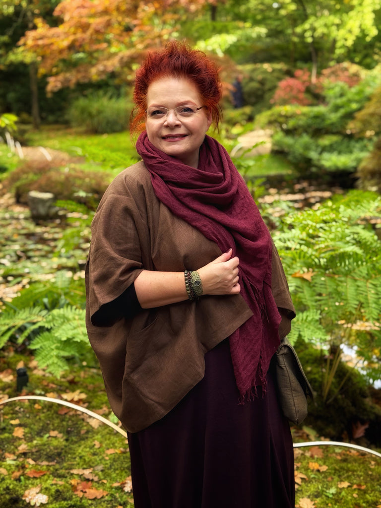 Woman with red hair wearing a brown poncho and maroon scarf in a garden setting