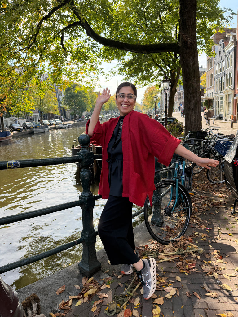 Person in a red jacket standing by a canal with bicycles in the background