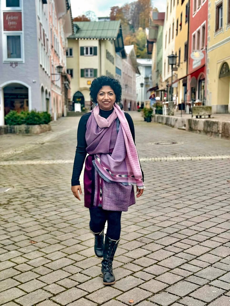 Woman walking wearing a purple cape on a cobblestone street in a European town with colorful buildings.