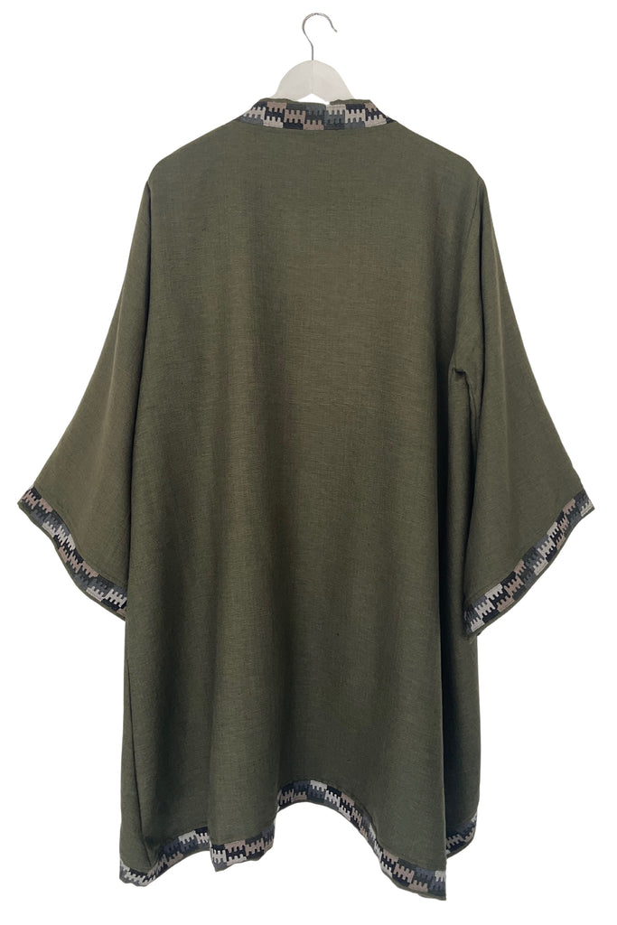Green poncho with patterned trim on a white background