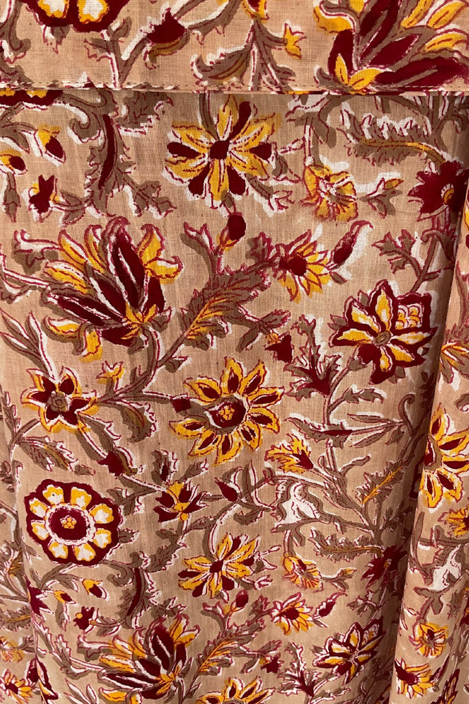 Close-up of a fabric with intricate floral patterns in brown, yellow, and red on a beige background.